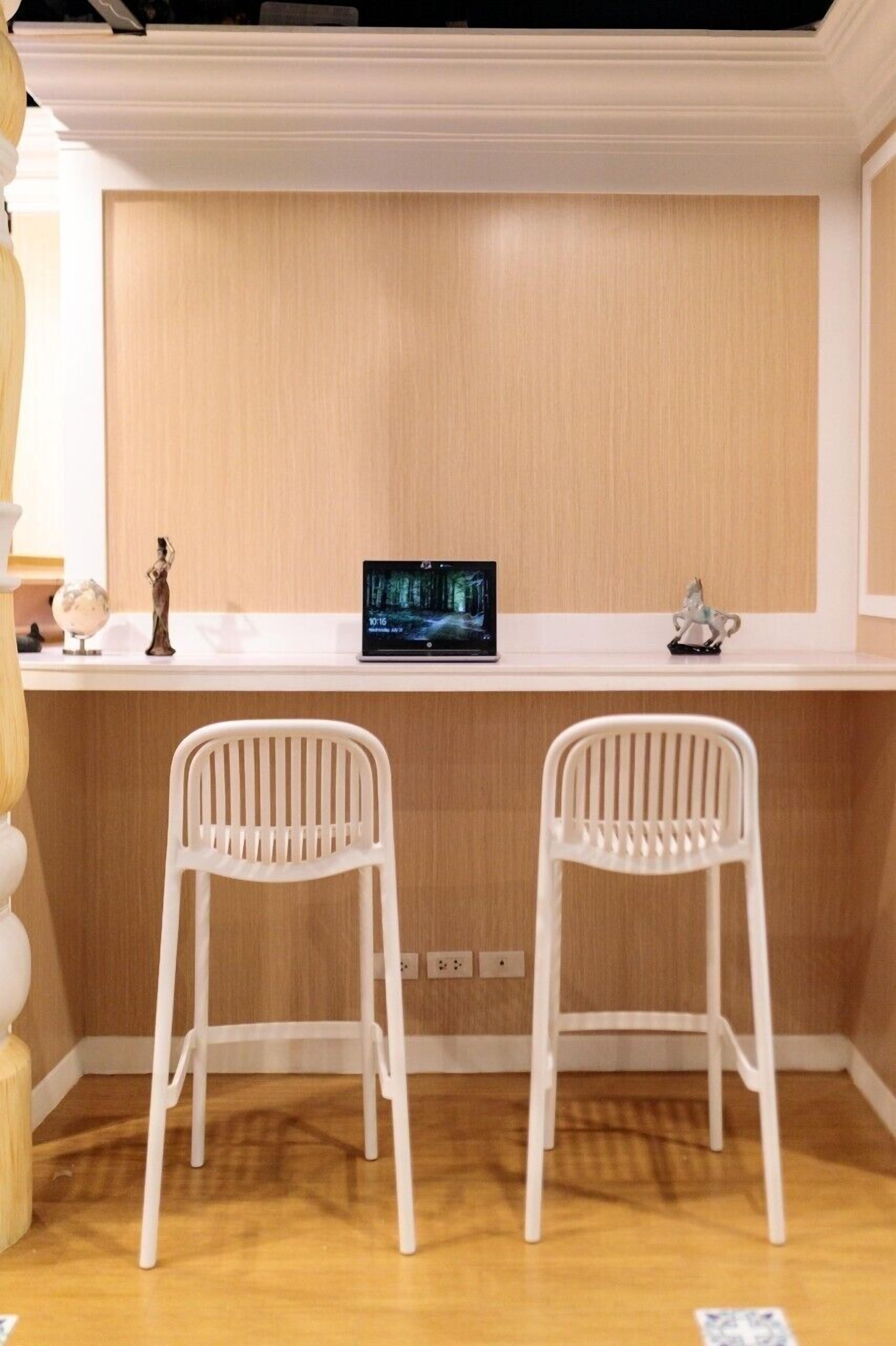 Una habitación con un escritorio blanco, dos sillas blancas, una computadora portátil y un globo terráqueo.