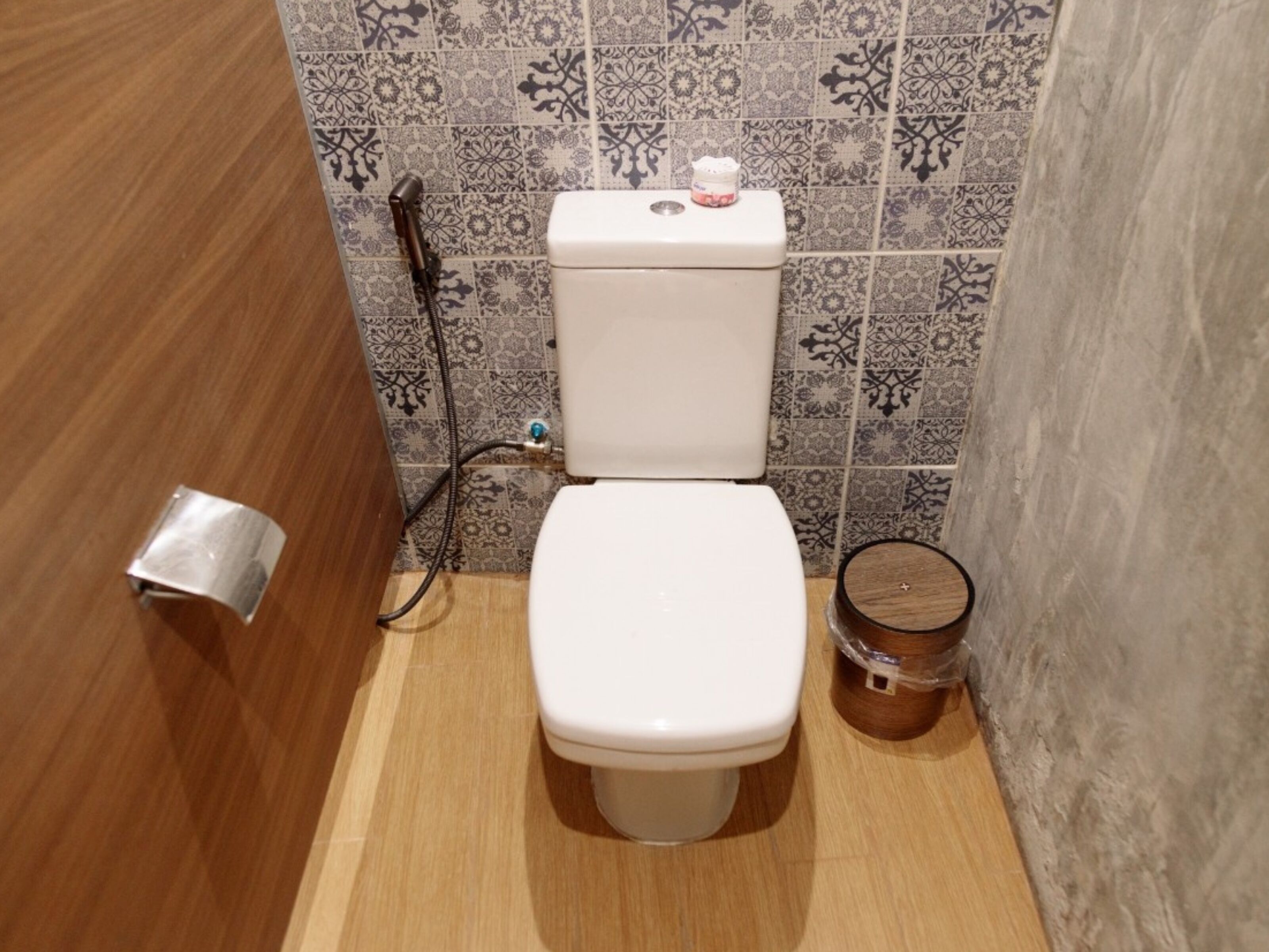 Ein kleines Badezimmer mit Toilette, Toilettenpapierhalter und einem Holz-Eimer.