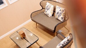 A room with a brown sofa set, two matching armchairs, and a small table with a cushion. - ReRe Hostel (Bangkok)