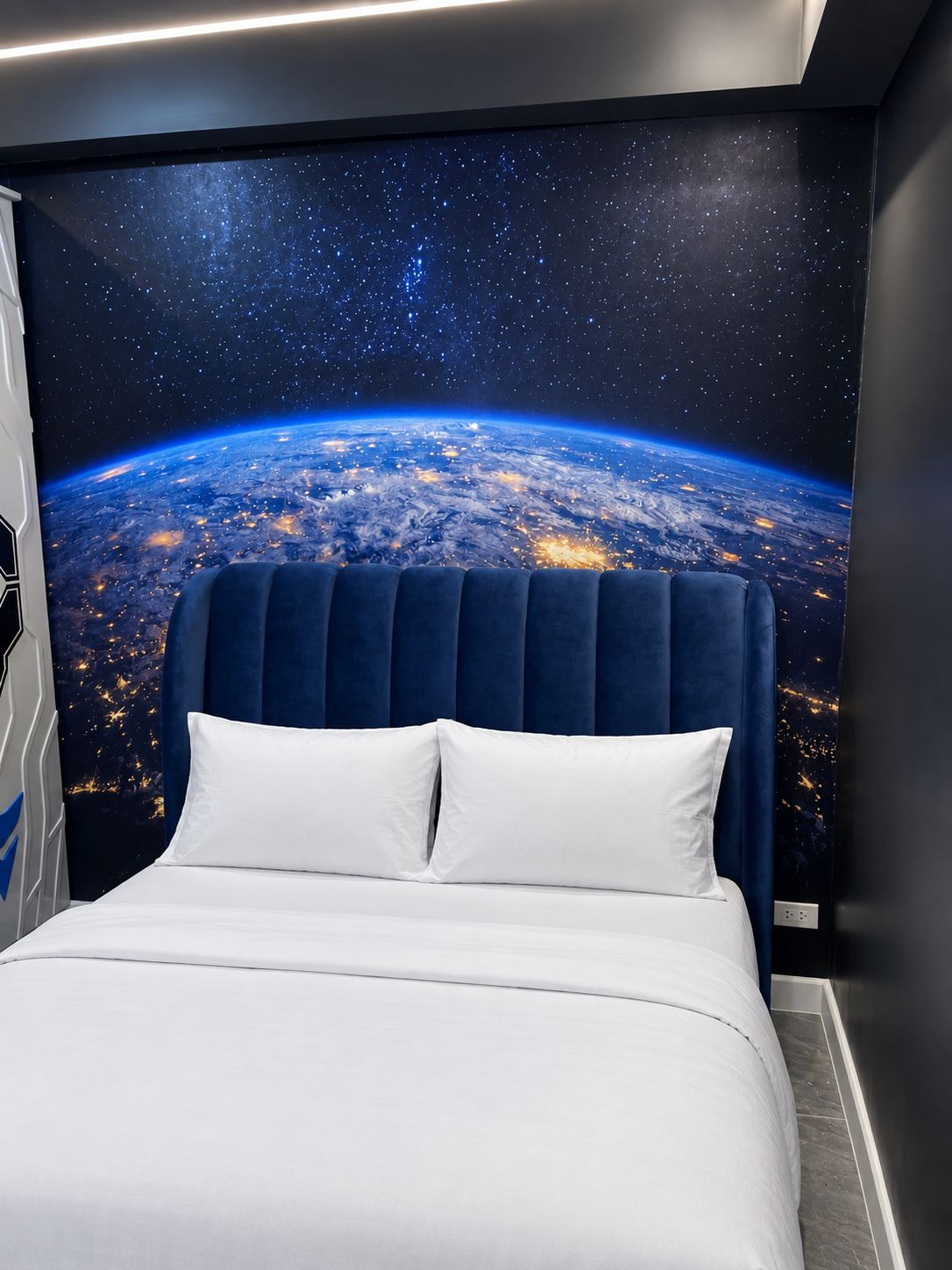A bed with a headboard against a wall with a space-themed mural.