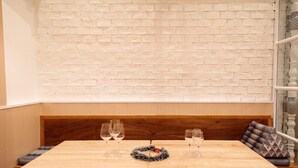 A dining area with a wooden table set for two, a white brick wall, and a wooden bench with cushions. - ReRe Hostel (Bangkok)