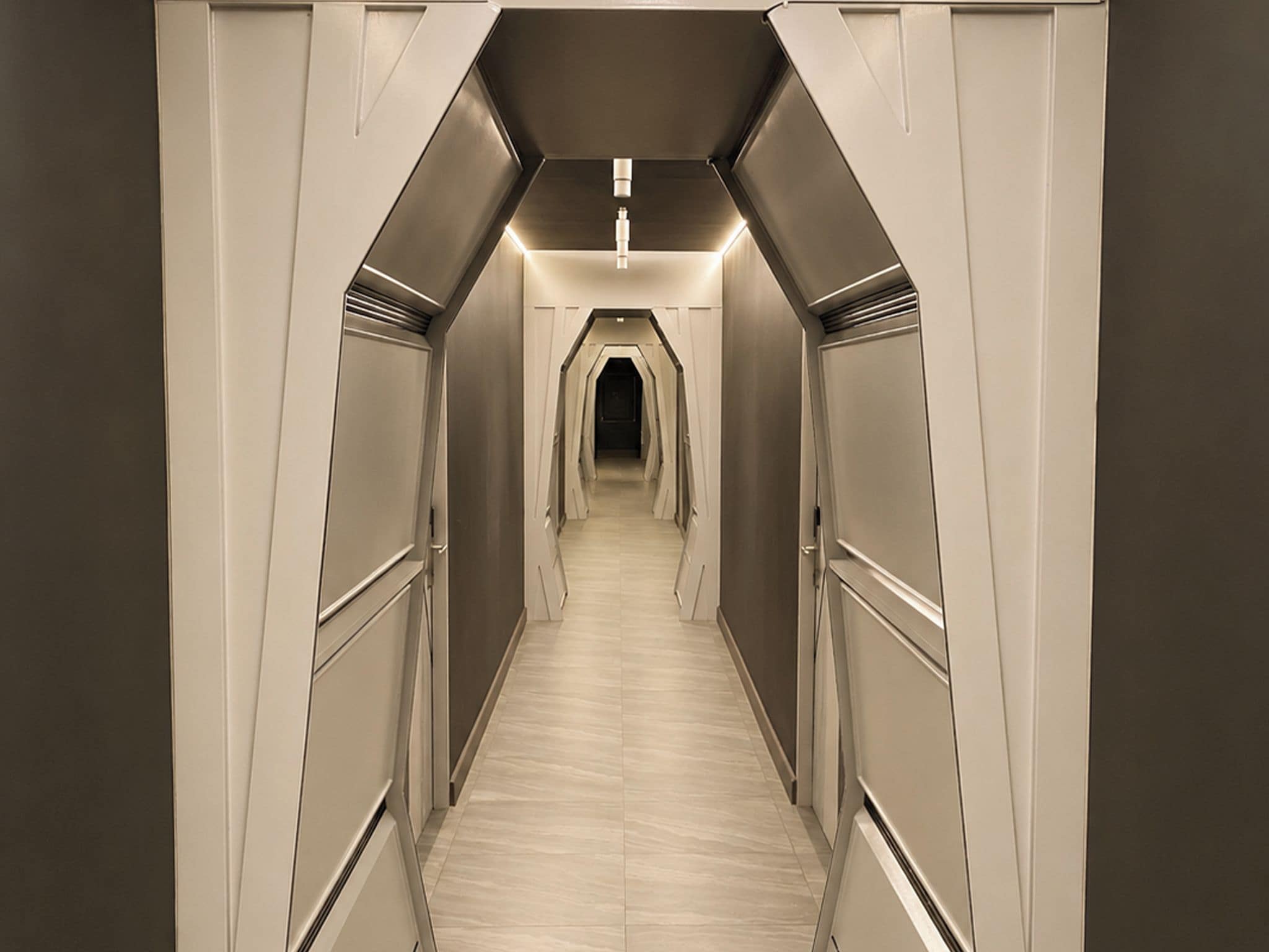 A modern, narrow hallway with a symmetrical design, featuring a central light fixture and a darkened end.