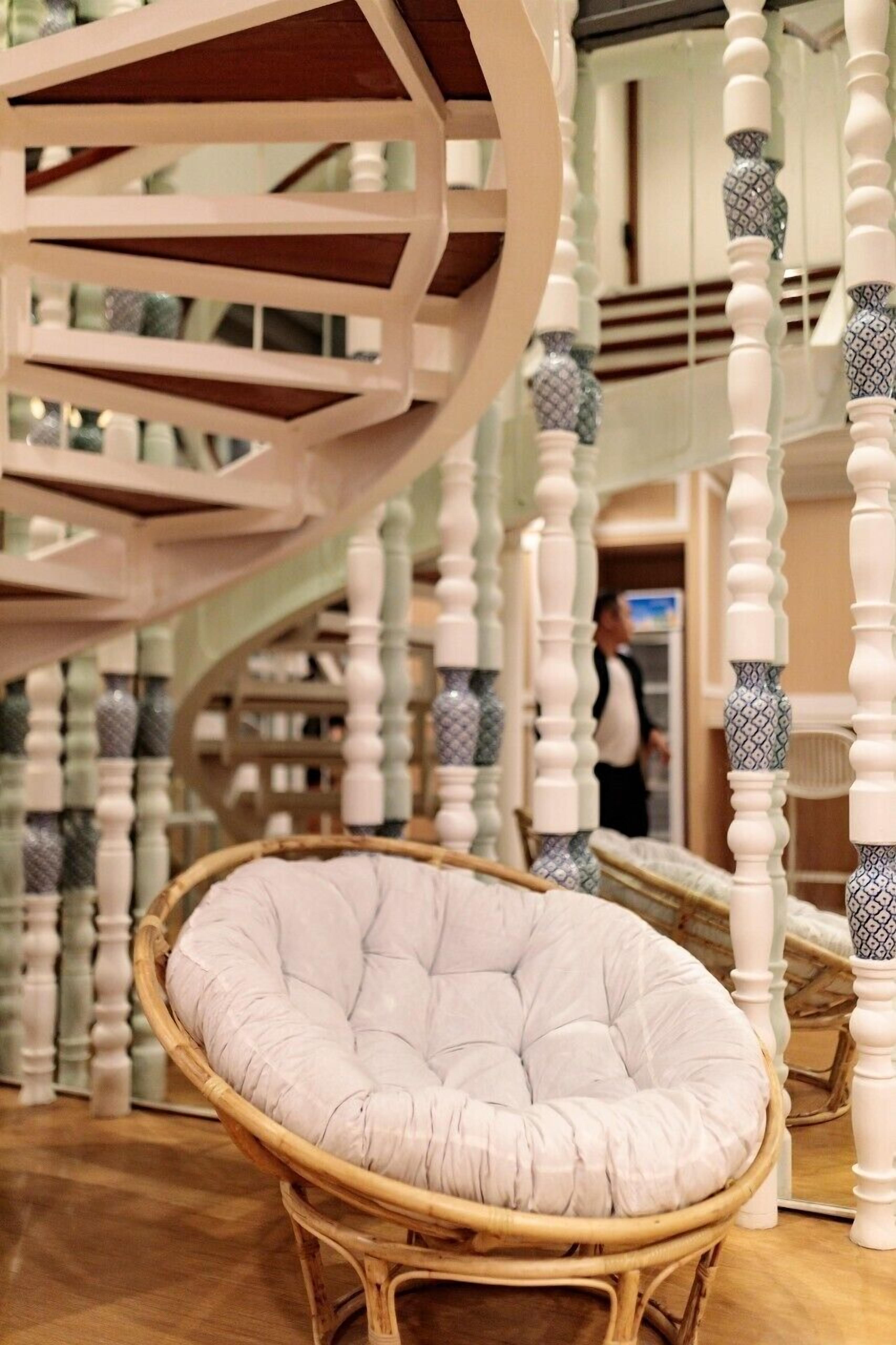 A spiral staircase with white and patterned balusters, a wicker chair, and a person in the background.