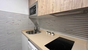 A kitchen with striped backsplash tiles, a stainless steel sink, a built-in oven, and a black induction cooktop. - Mena Trip Malaga- Studio in the historic center (Málaga)