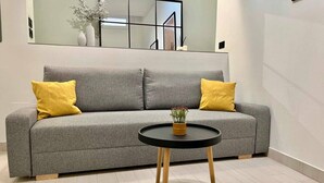 A grey sofa with two yellow pillows and a small round table with a plant. - Mena Trip Malaga- Studio in the historic center (Málaga)
