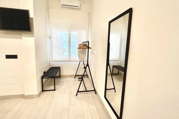 A hallway with a large mirror, a TV mounted on the wall, and a window with a view of trees.