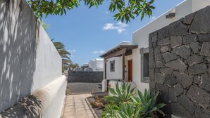 A narrow pathway between buildings with white walls and a stone wall, leading to a door.