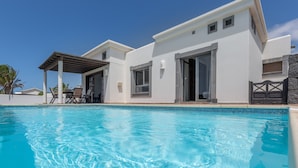 A modern house with a swimming pool, a covered patio, and a stone wall.