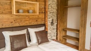 A bedroom with a wooden headboard, a stone accent wall, and a wooden shelf unit. - Apartment Almhütte SKI IN - SKI OUT (Brixen im Thale)