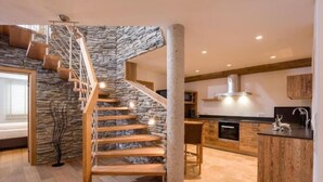 A modern kitchen with a stone wall staircase, wooden flooring, and built-in appliances. - Apartment Almhütte SKI IN - SKI OUT (Brixen im Thale)