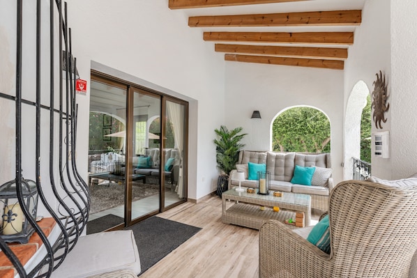 A spacious patio with wicker furniture, a glass door leading to an outdoor seating area, and a view of greenery.