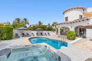 A swimming pool with a hot tub, lounge chairs, and a covered patio area.