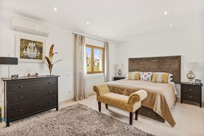 A bedroom with a bed, a dresser, a bench, a nightstand, and a window with curtains.