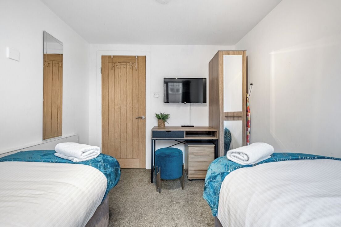 Una habitación de hotel con dos camas, un escritorio con computadora, un televisor y un armario.