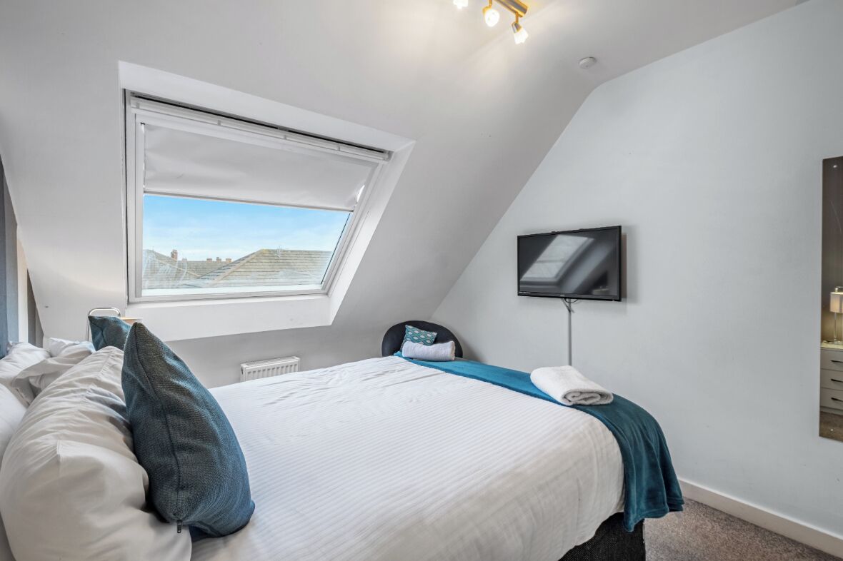 Un dormitorio con tragaluz, una cama con almohadas, un televisor de pantalla plana montado en la pared y vistas al exterior.