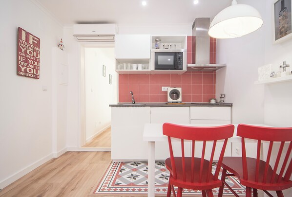 A modern kitchen with white cabinets, a microwave, and a sink. There are two red chairs at a white table.