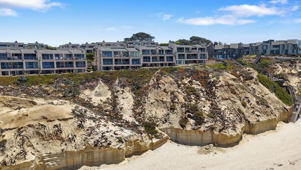 Un hotel costero con varias construcciones, una playa de arena y un acantilado rocoso con vegetación.