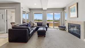 Una sala de estar moderna con un sofá modular, una chimenea y ventanas grandes que ofrecen vistas al exterior.