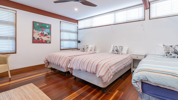 Un dormitorio con dos camas, piso de madera, ventilador de techo y un cuadro en la pared.