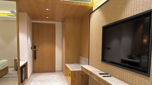 Une chambre d’hôtel moderne dotée d’un grand téléviseur à écran plat fixé sur un mur texturé, d’une porte en bois et d’un petit coin salon avec un banc.