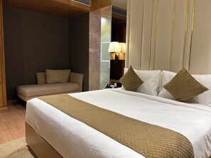 A hotel room with a large bed, a sofa, a bedside table with a lamp, and a mirror. - Hotel Grand Imperia (Raipur)