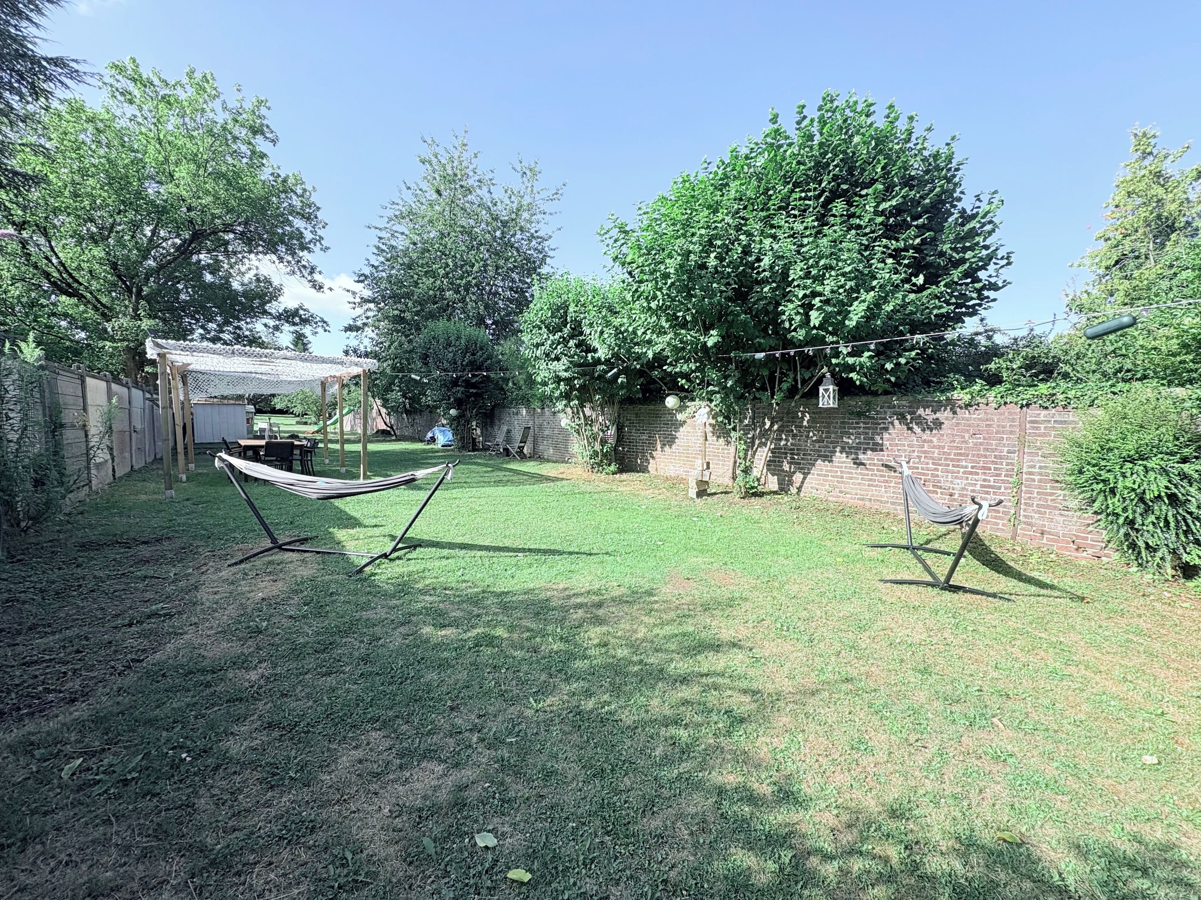 A backyard with a hammock, a pergola, and a brick wall.