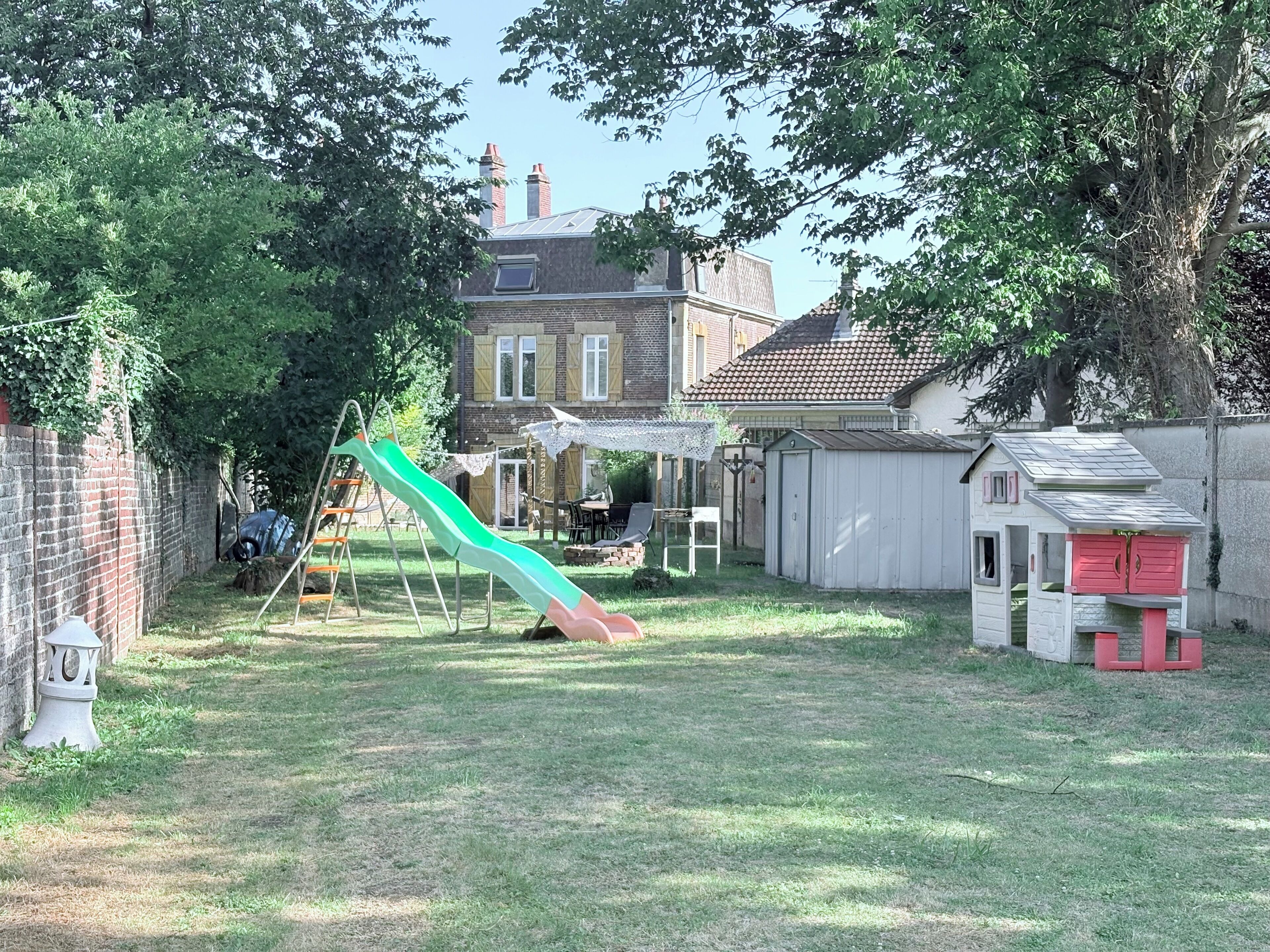 Ein Garten mit Rutsche, einem kleinen Schuppen und einem Haus im Hintergrund.
