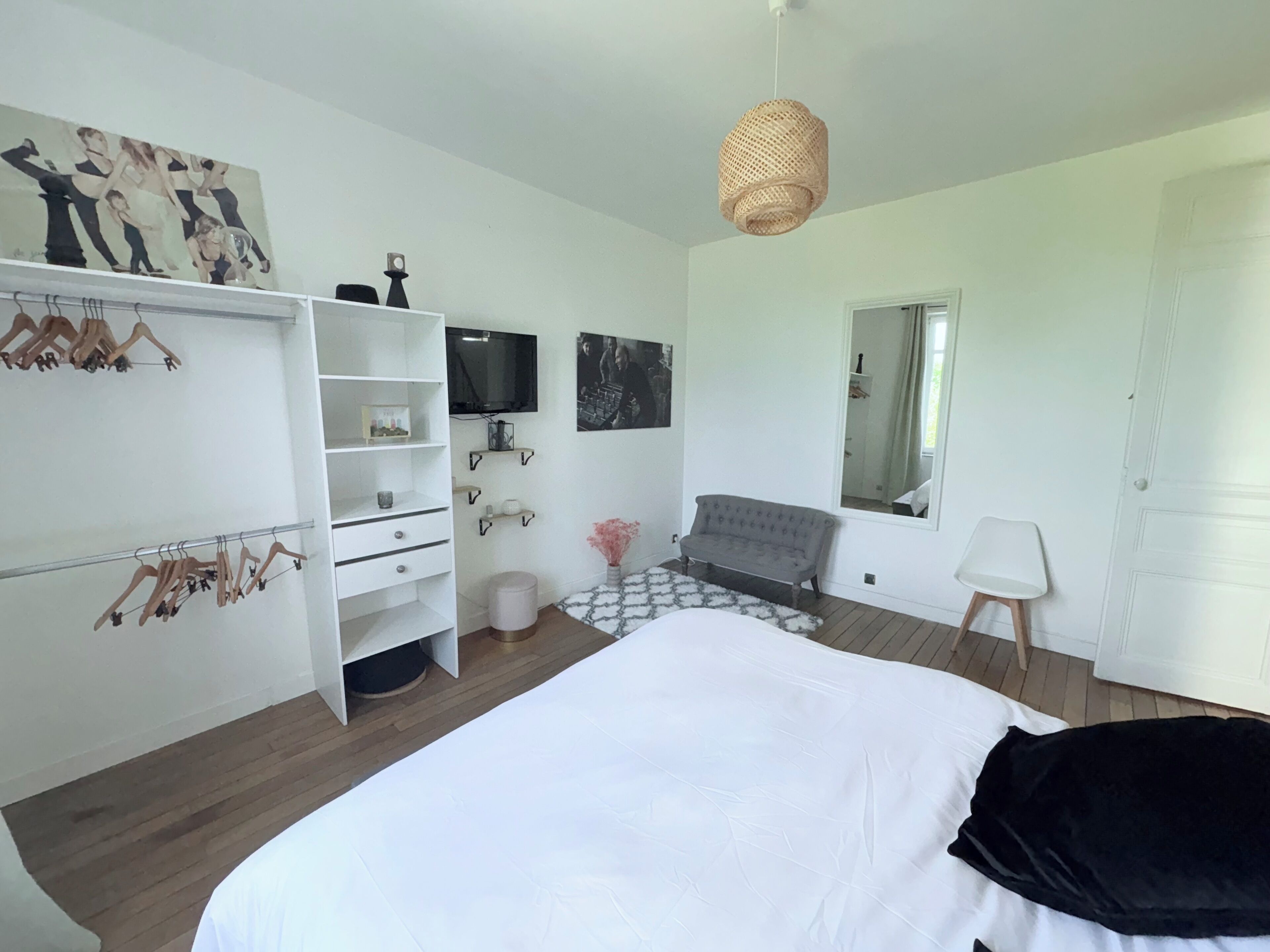 Une chambre à coucher comprenant un lit, une armoire, un téléviseur, un miroir et un luminaire suspendu.