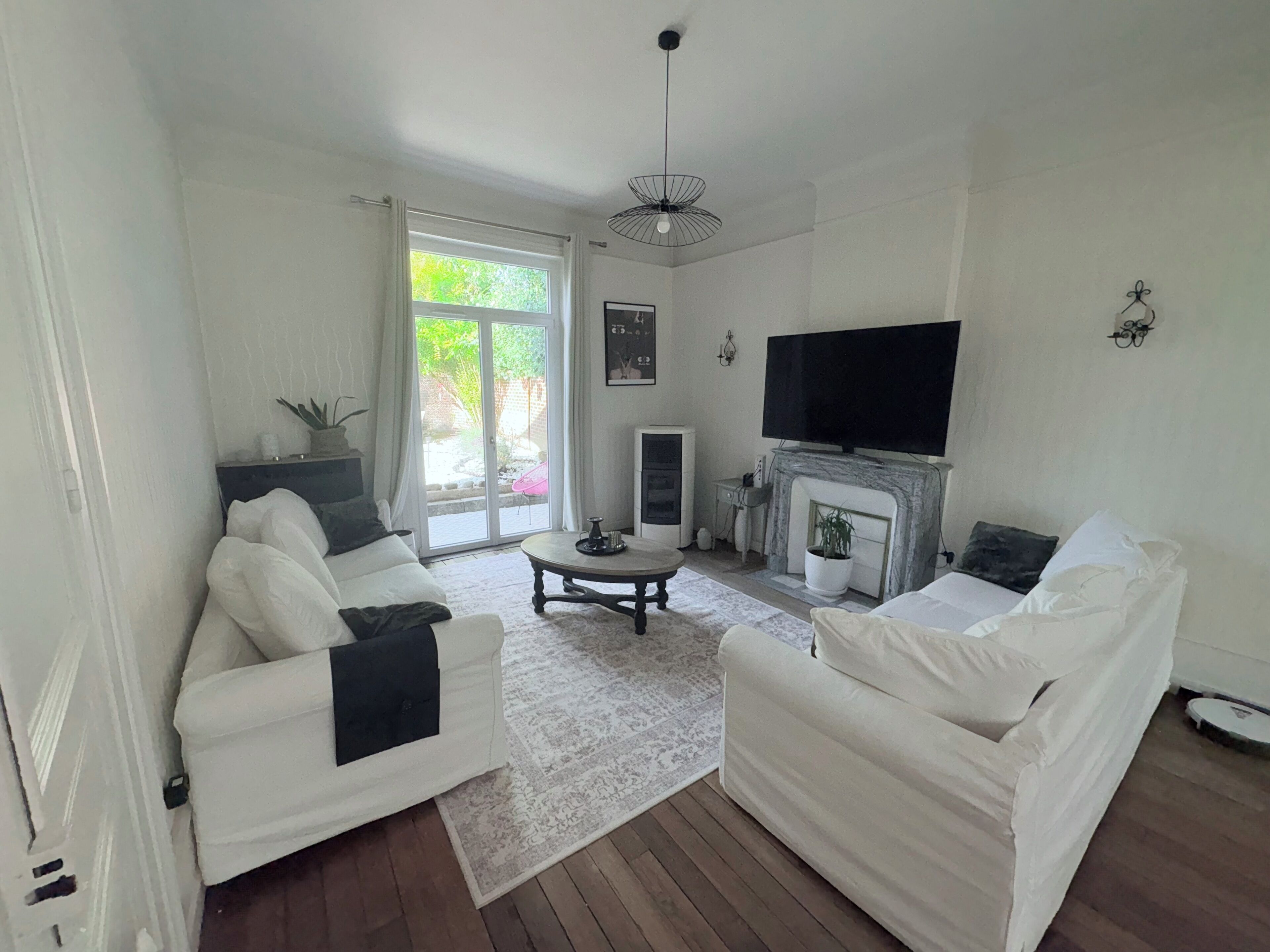 Una sala de estar con dos sofás blancos, una mesa de centro, una chimenea, un televisor y un ventanal corredera que da a un área exterior.