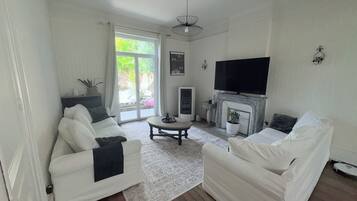 Una sala de estar con dos sofás blancos, una mesa de centro, una chimenea, un televisor y un ventanal corredera que da a un área exterior.