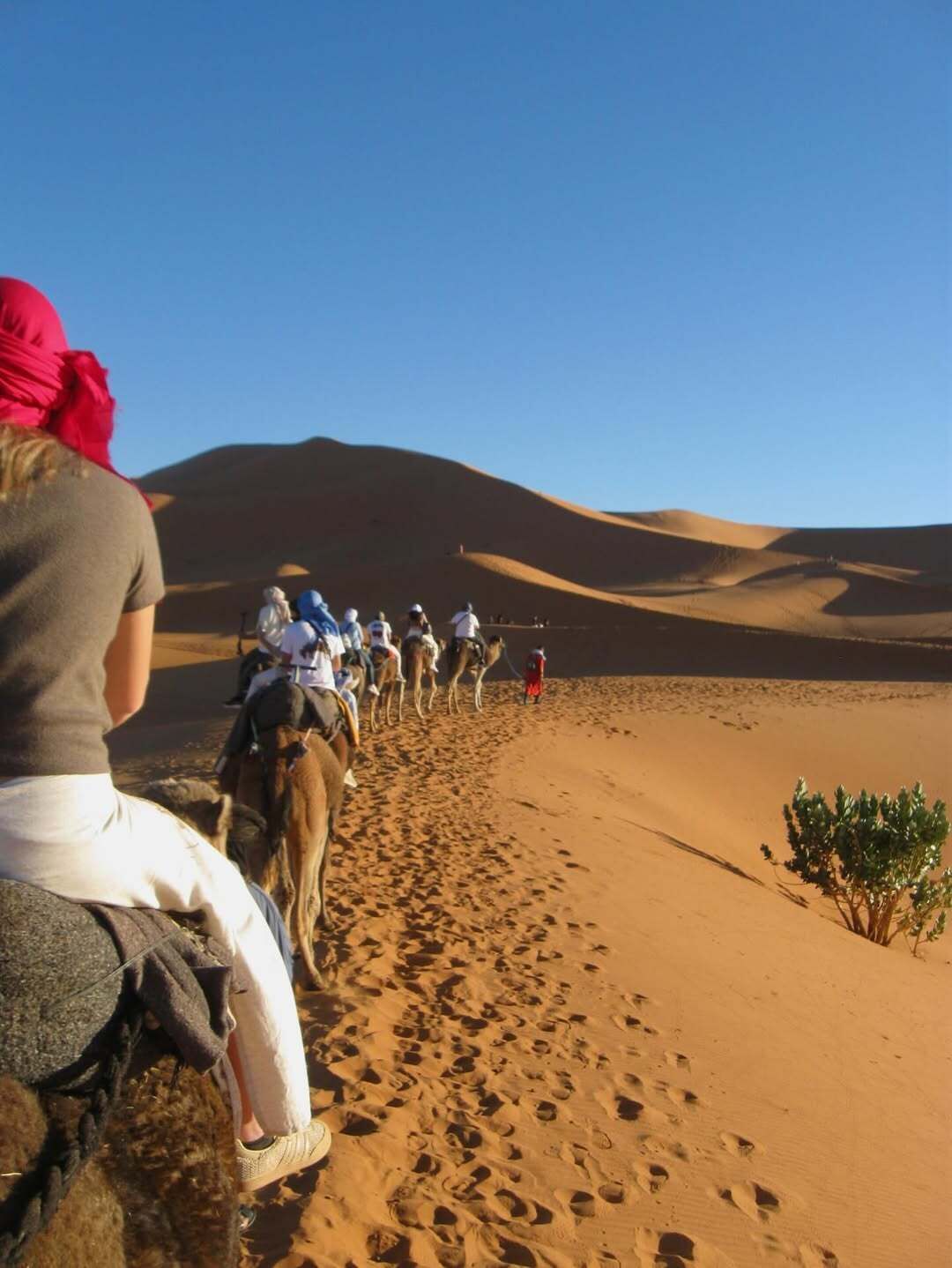 A desert landscape with sand dunes and a group of people riding camels.