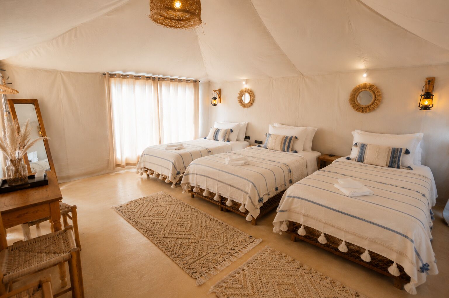 A tent-style room with three beds, a wooden desk, and a mirror.