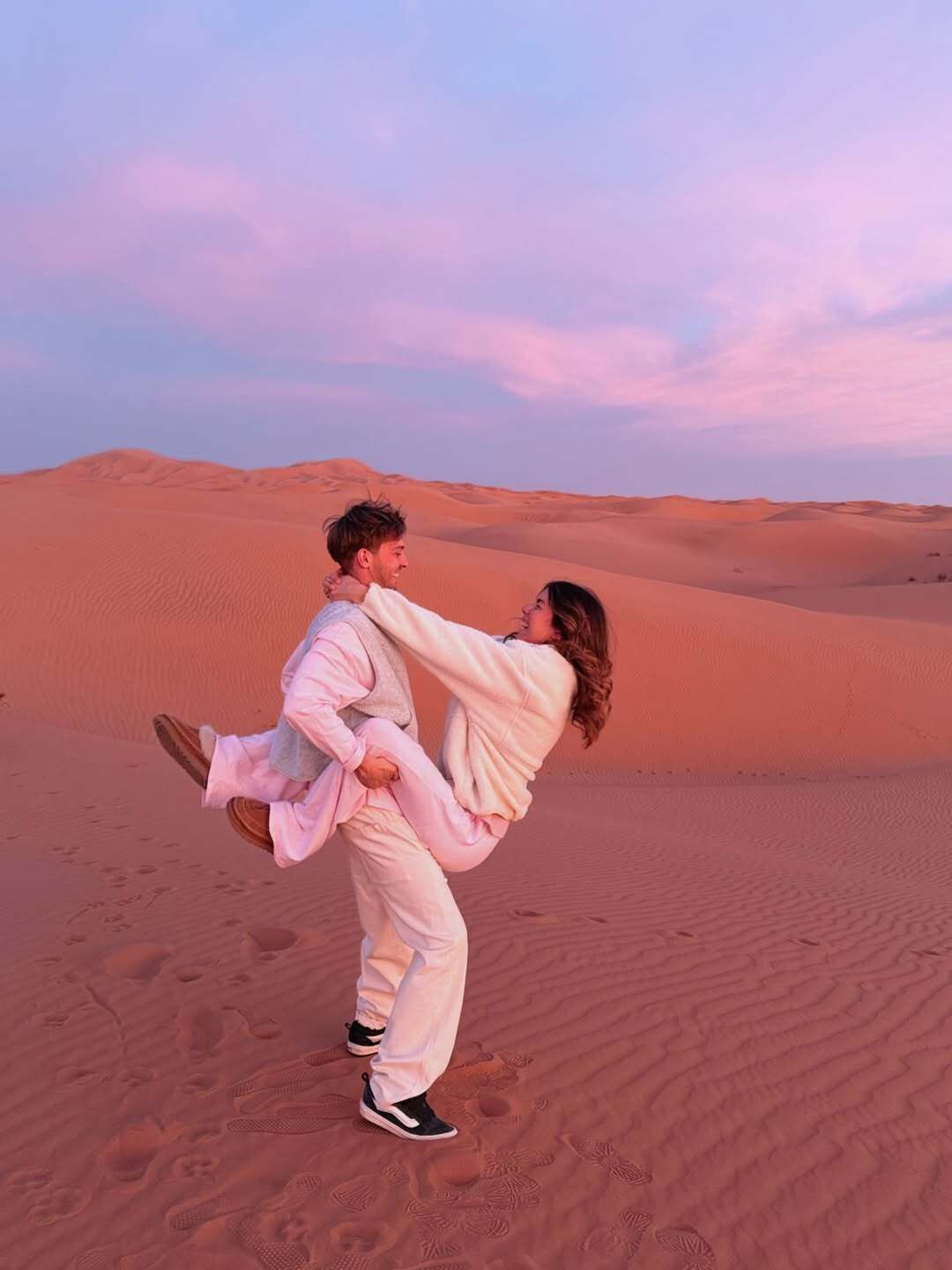 Una pareja en un paisaje desértico con dunas de arena al fondo.