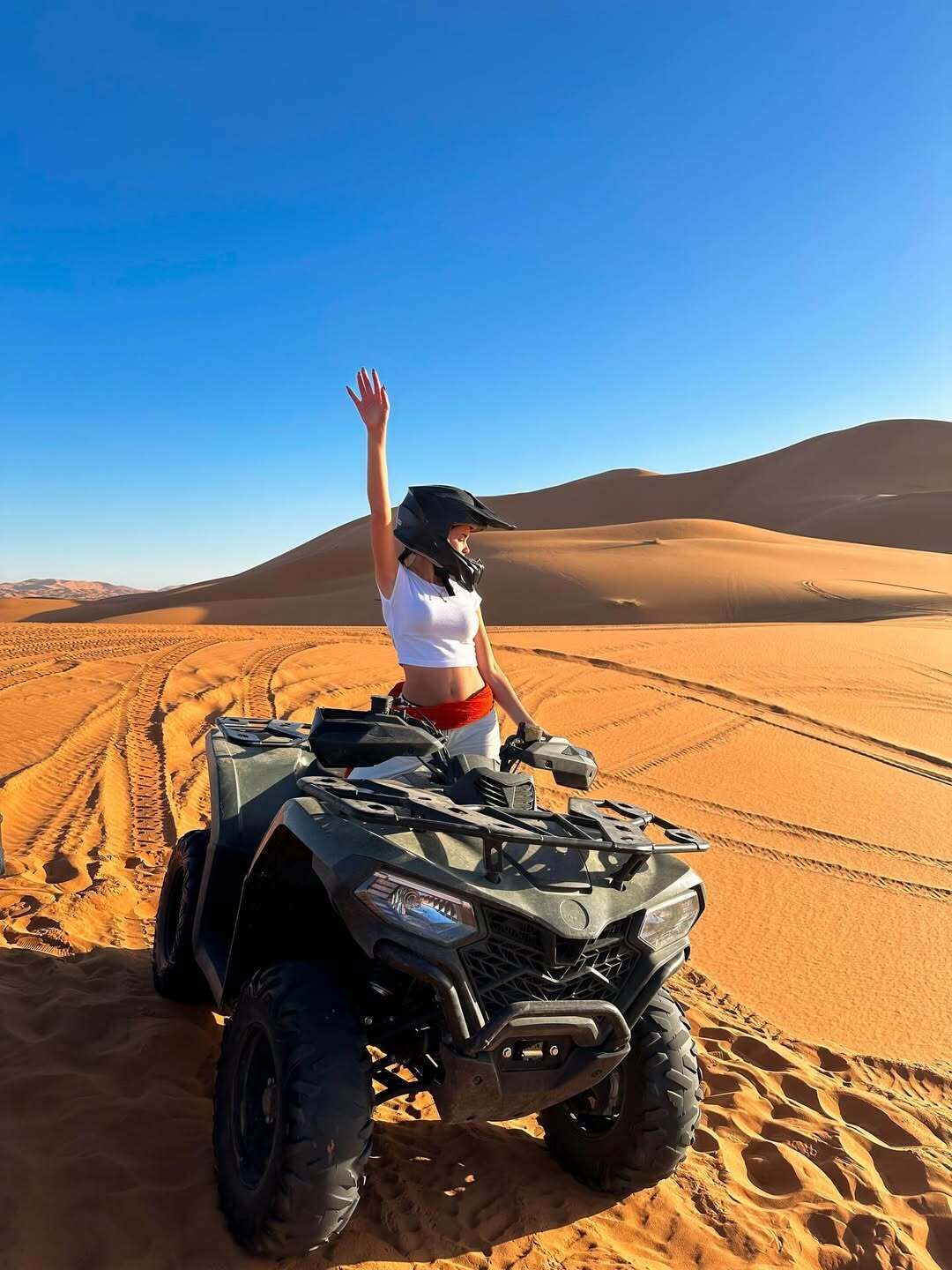 Una persona manejando un vehículo todo terreno en un desierto, con dunas de arena al fondo.
