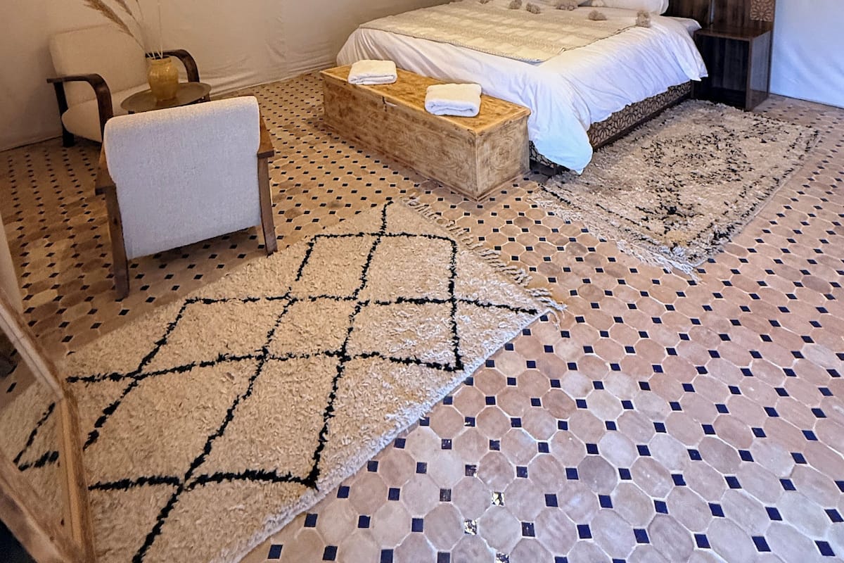 Een slaapkamer met een bed, nachtkastje, stoel, vloerkleed en een hanglamp.