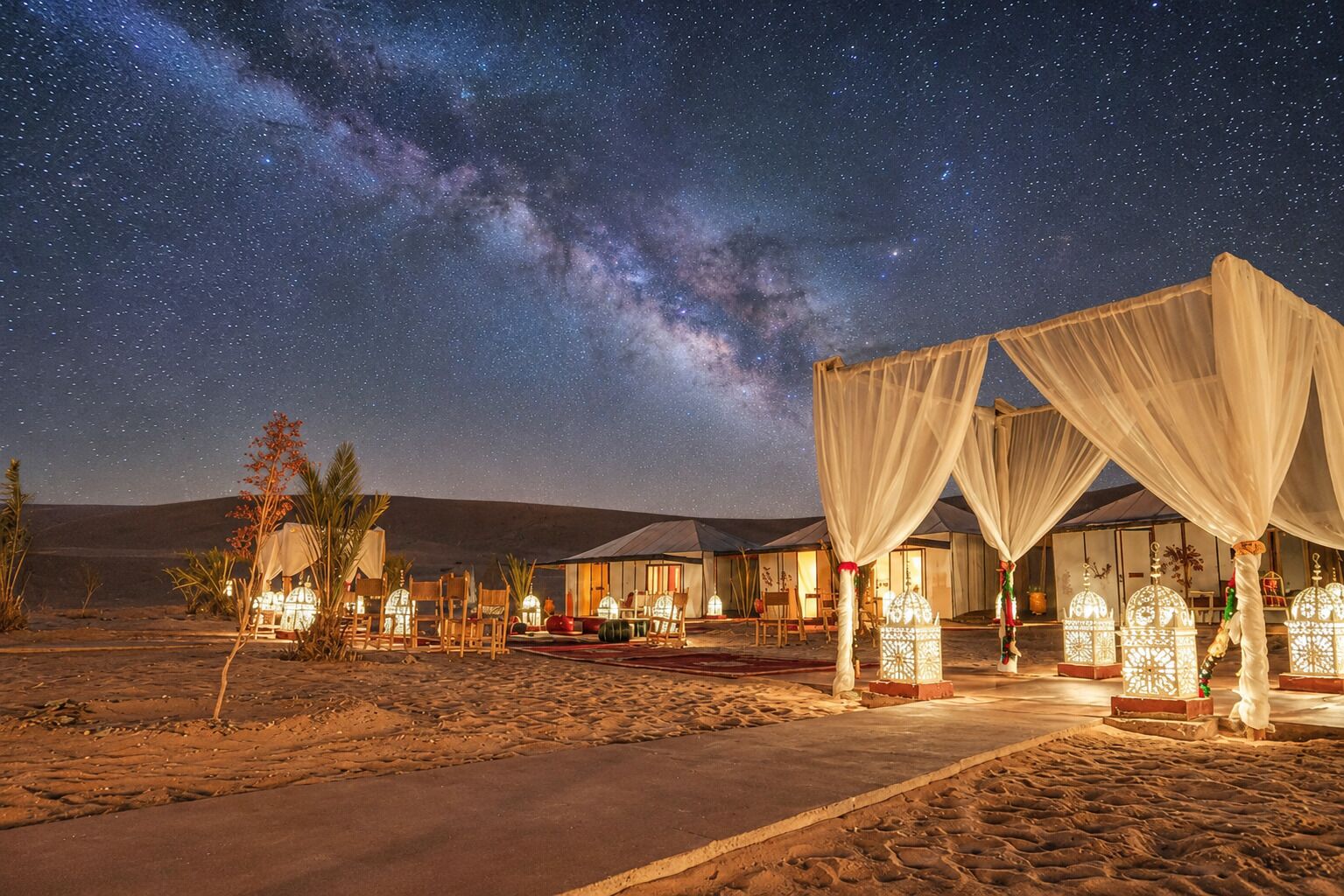 Un resort en el desierto con tiendas de campaña, cielo estrellado y faroles iluminados.