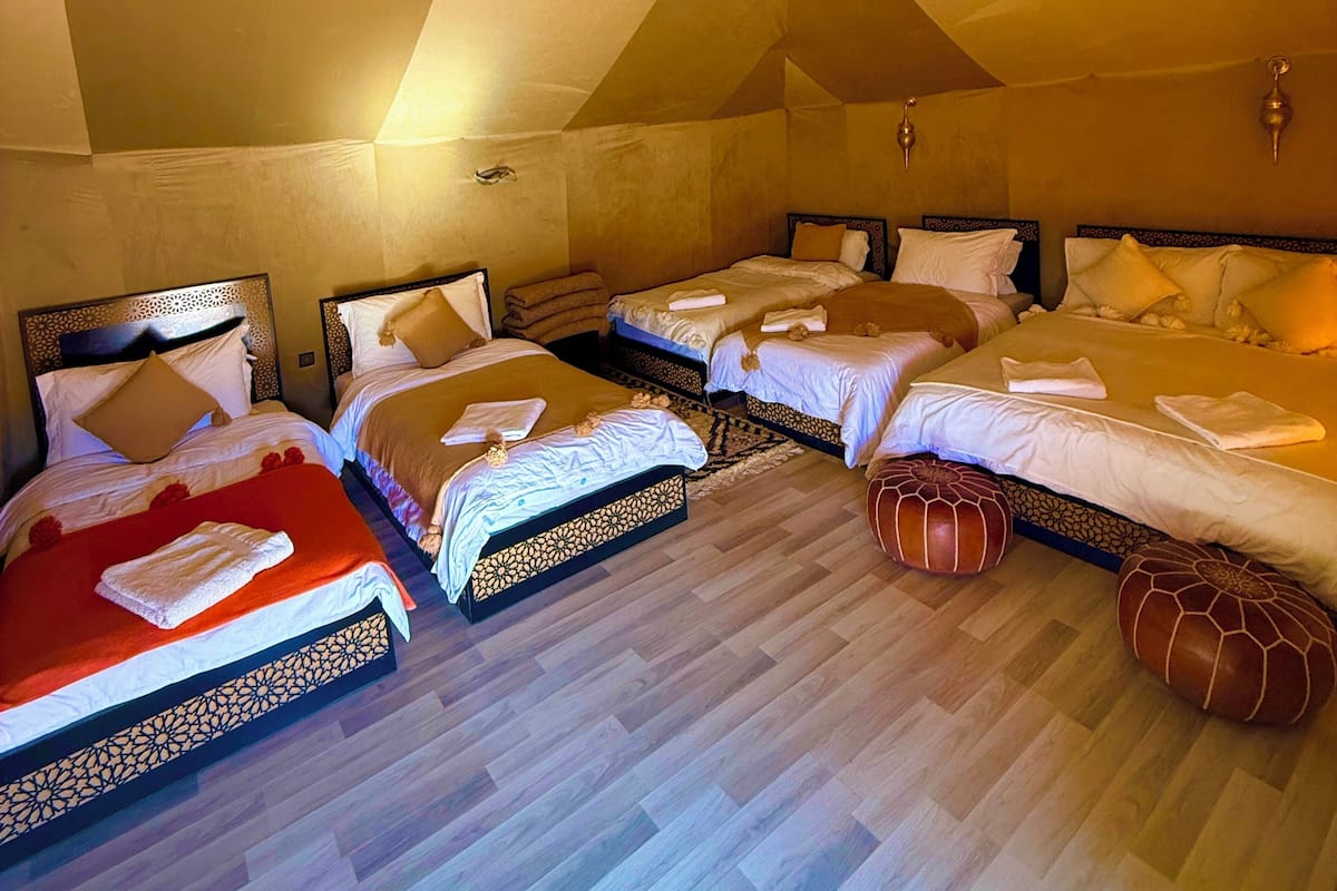 Een hotelkamer met vier bedden op rij, een houten vloer en twee hangende lampen.