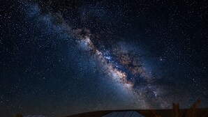 A starry night sky with a visible Milky Way, a building with large windows, and outdoor seating with lanterns.