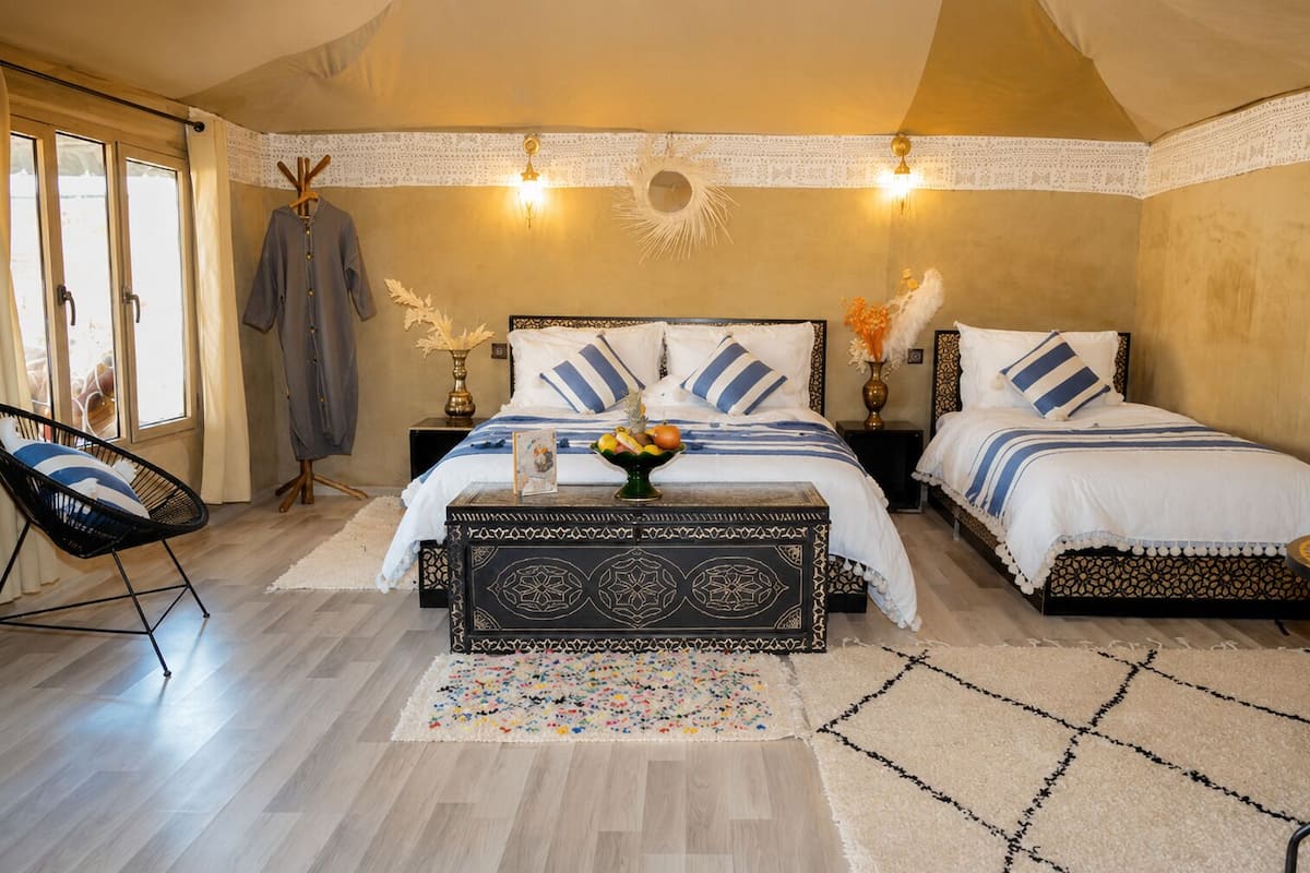 Un dormitorio con dos camas, una silla, un banco decorativo y un adorno de pared con forma de sol.