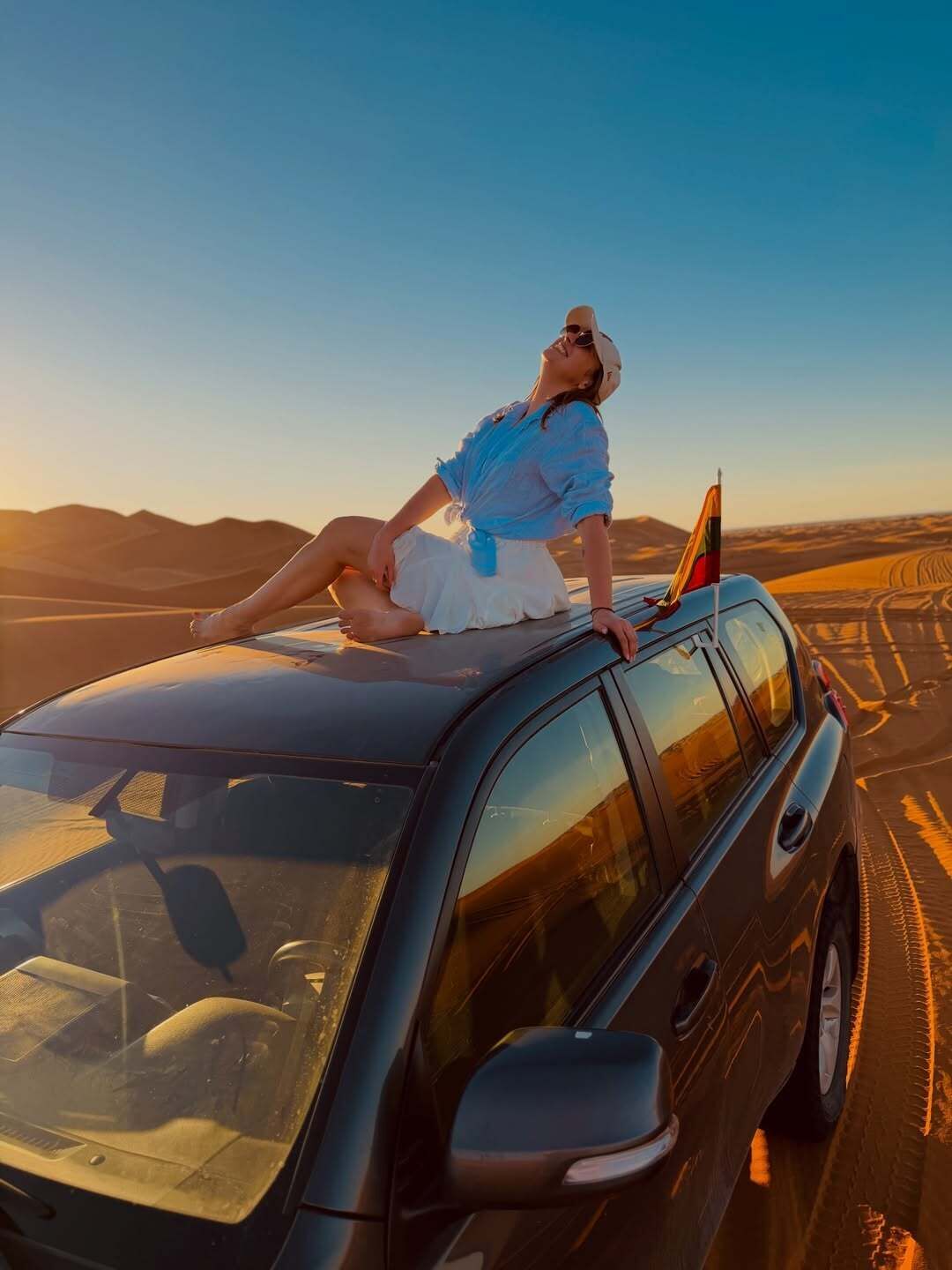 Una persona sentada sobre el techo de un coche con un paisaje desértico al fondo.