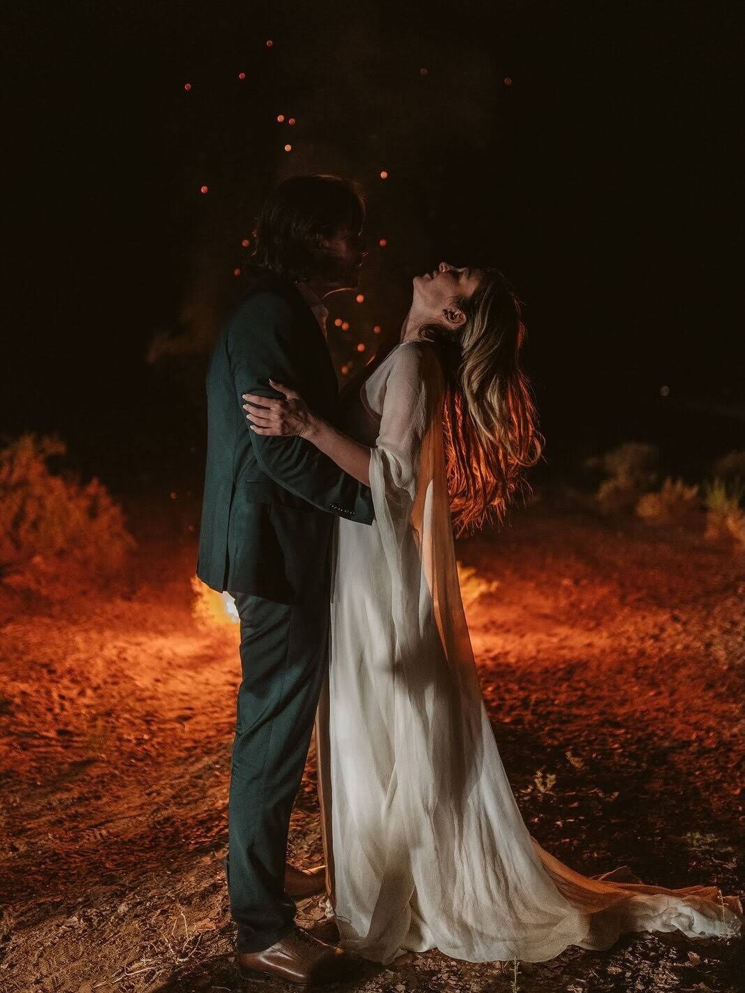 A couple embracing in a dimly lit outdoor setting with a ground covered in dry leaves.