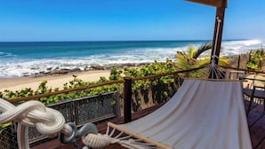 Une vue sur la plage depuis une terrasse couverte, avec un hamac et des cordes.