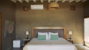 Une chambre avec un grand lit, deux tables de chevet, un climatiseur fixé au mur, un luminaire suspendu et un tableau accroché au mur.