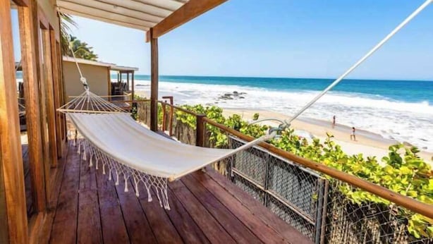 Une terrasse en bois avec un hamac donnant sur une plage.