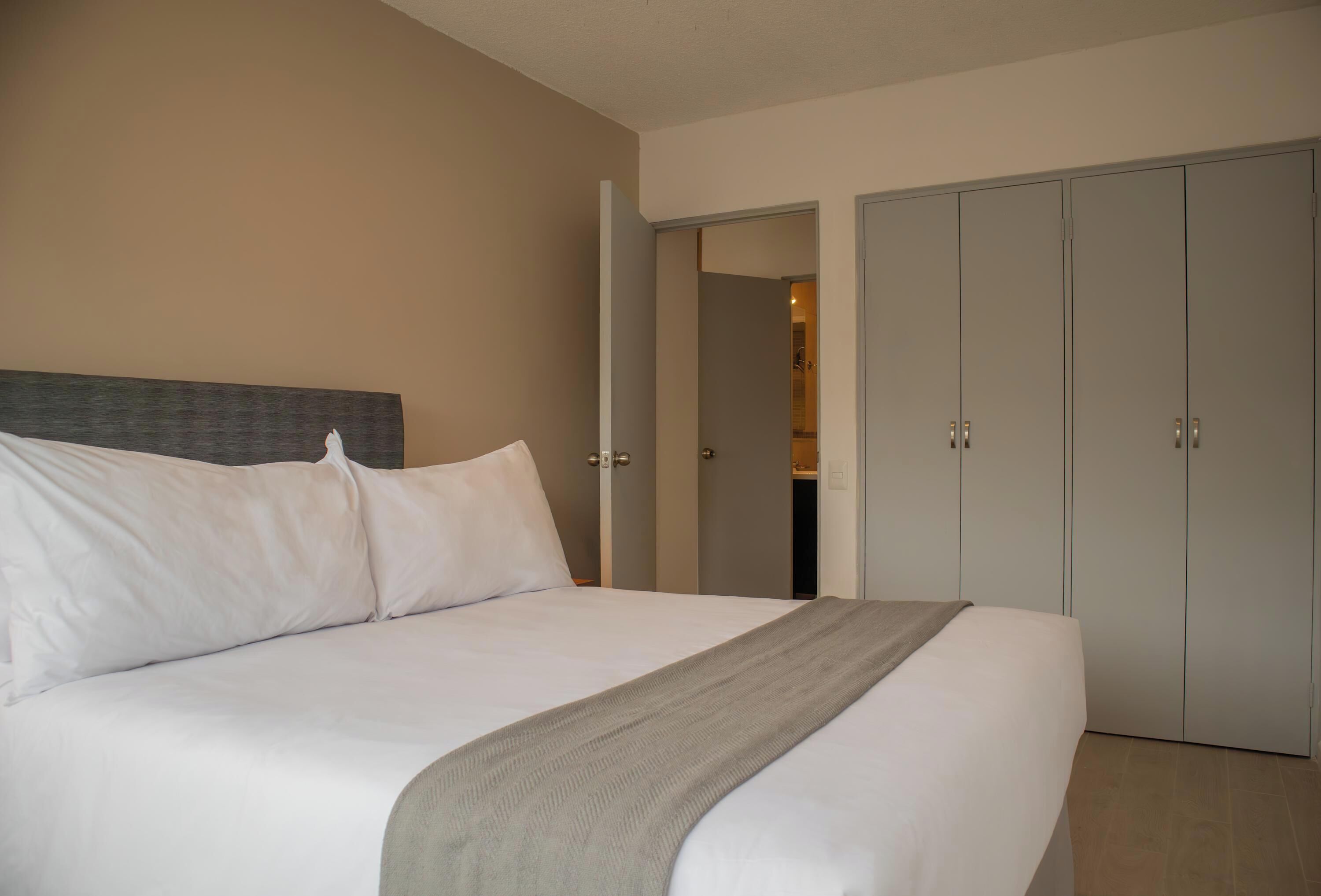 A hotel room with a large bed, a grey blanket, and a wardrobe with multiple doors.