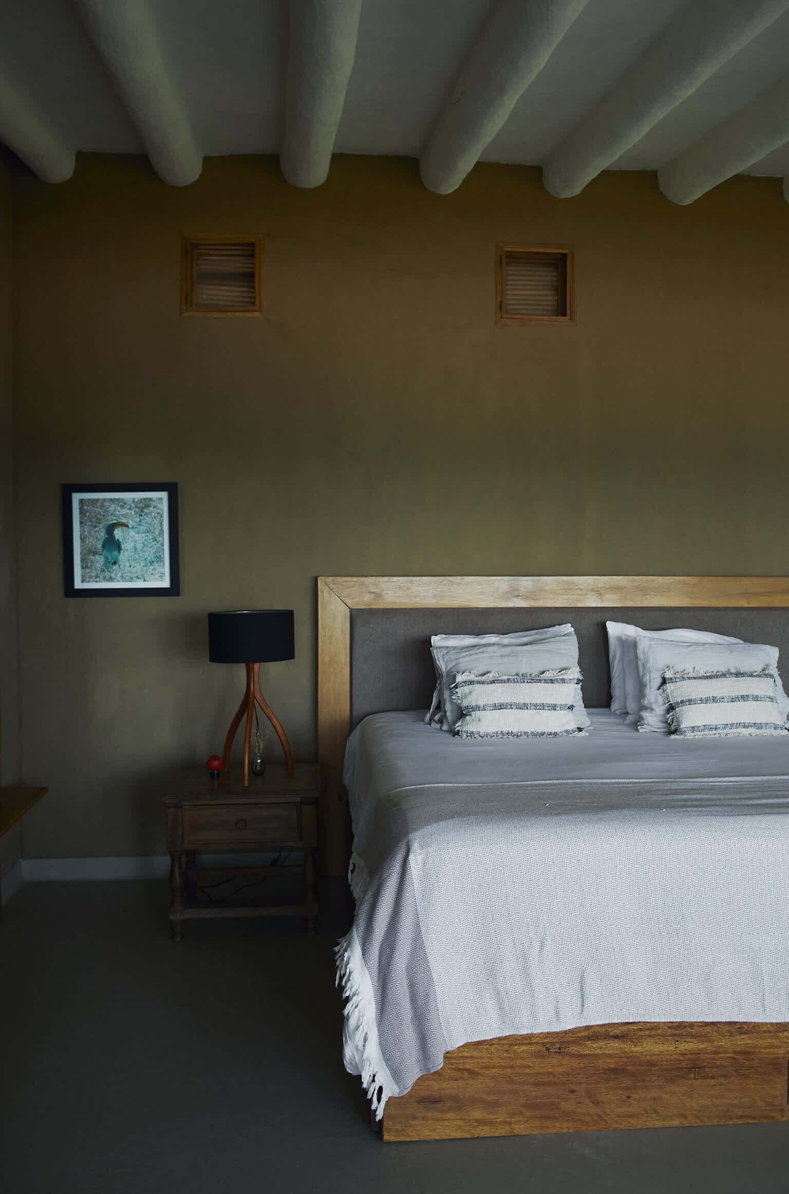 A bedroom with a wooden headboard, a bed with white bedding, a nightstand with a lamp, and a framed picture on the wall.