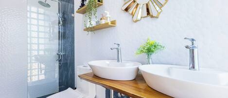 Un baño moderno con ducha de vidrio, inodoro y dos lavamanos sobre una encimera de madera.