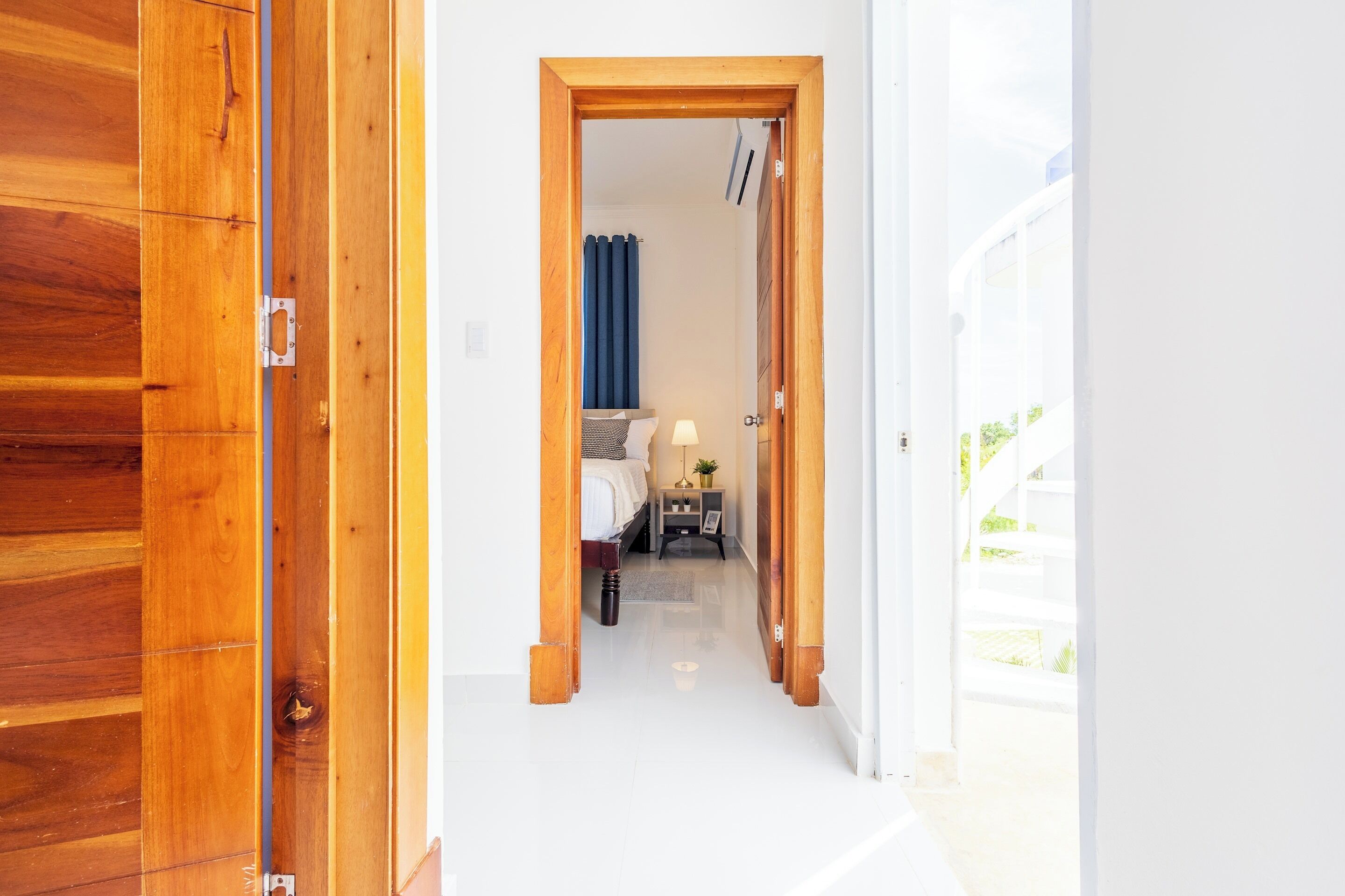 Un pasillo que conduce a un dormitorio con cama, mesita de noche y lámpara.