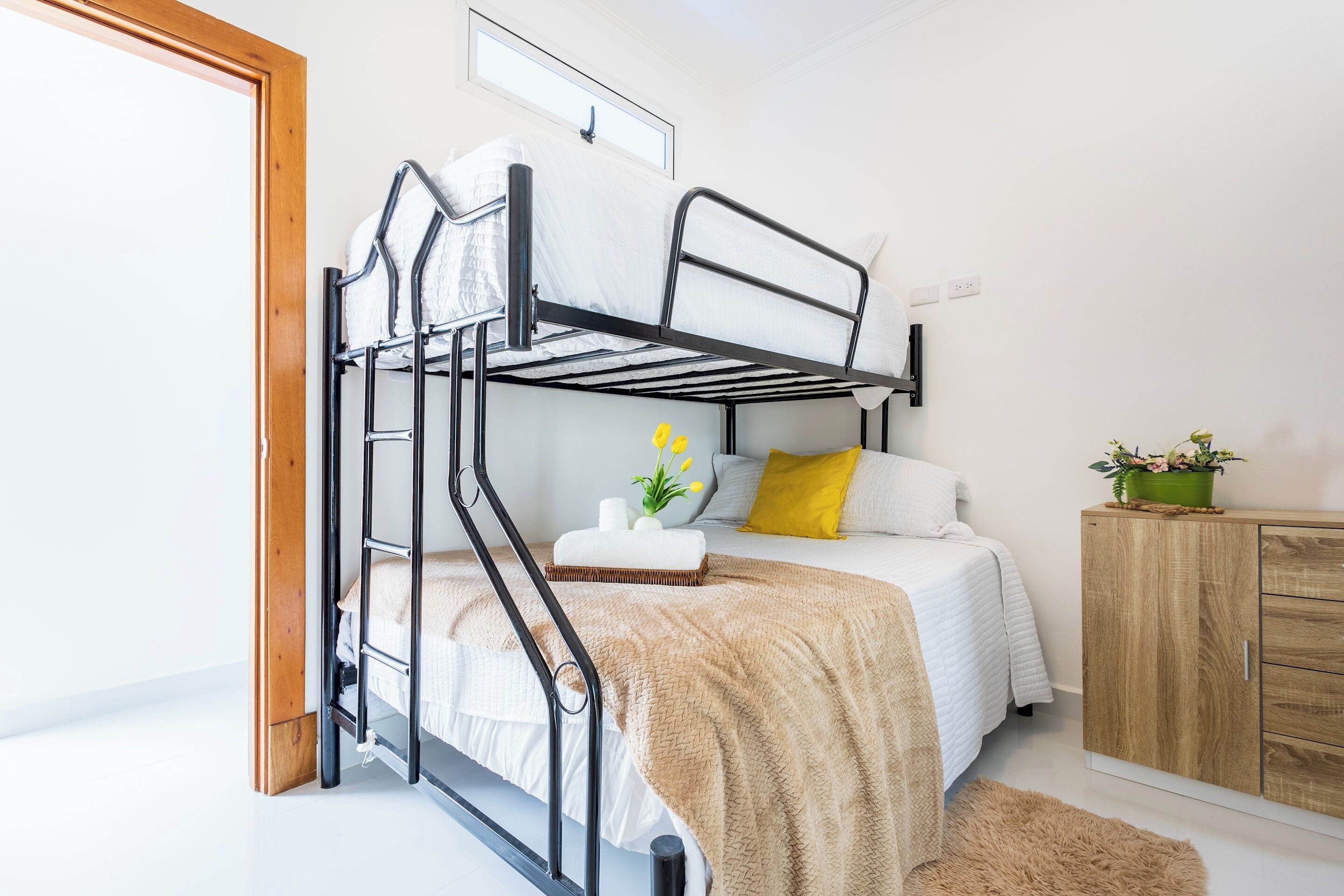 A bunk bed with a white mattress, a wooden cabinet, and a small plant on the side.