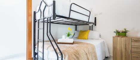 A bunk bed with a white mattress, a wooden cabinet, and a small plant on the side.